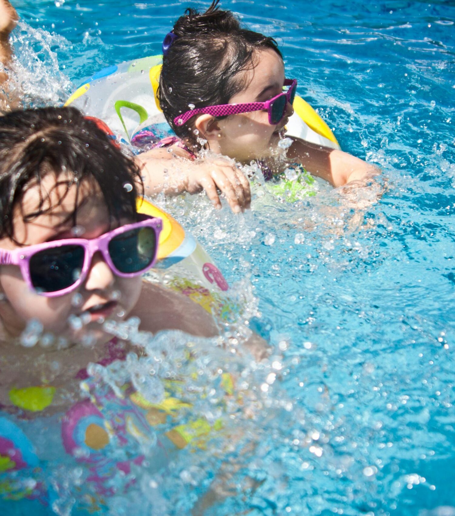 Two young girls enjoying a playful day in a bright blue swimming pool with colorful float rings.