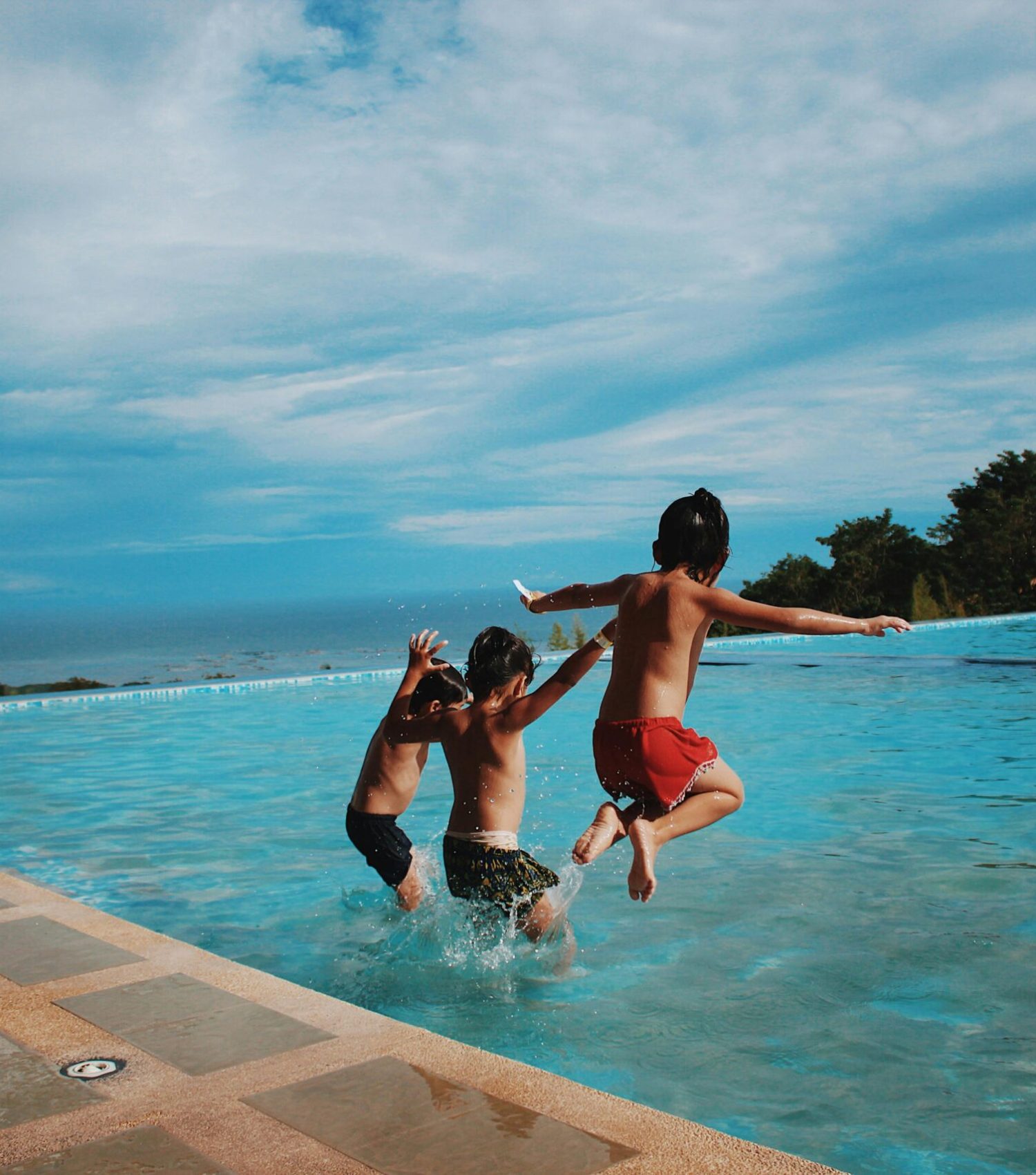 Two children joyfully jump into a pool on a sunny day, embodying excitement and summer vibes.